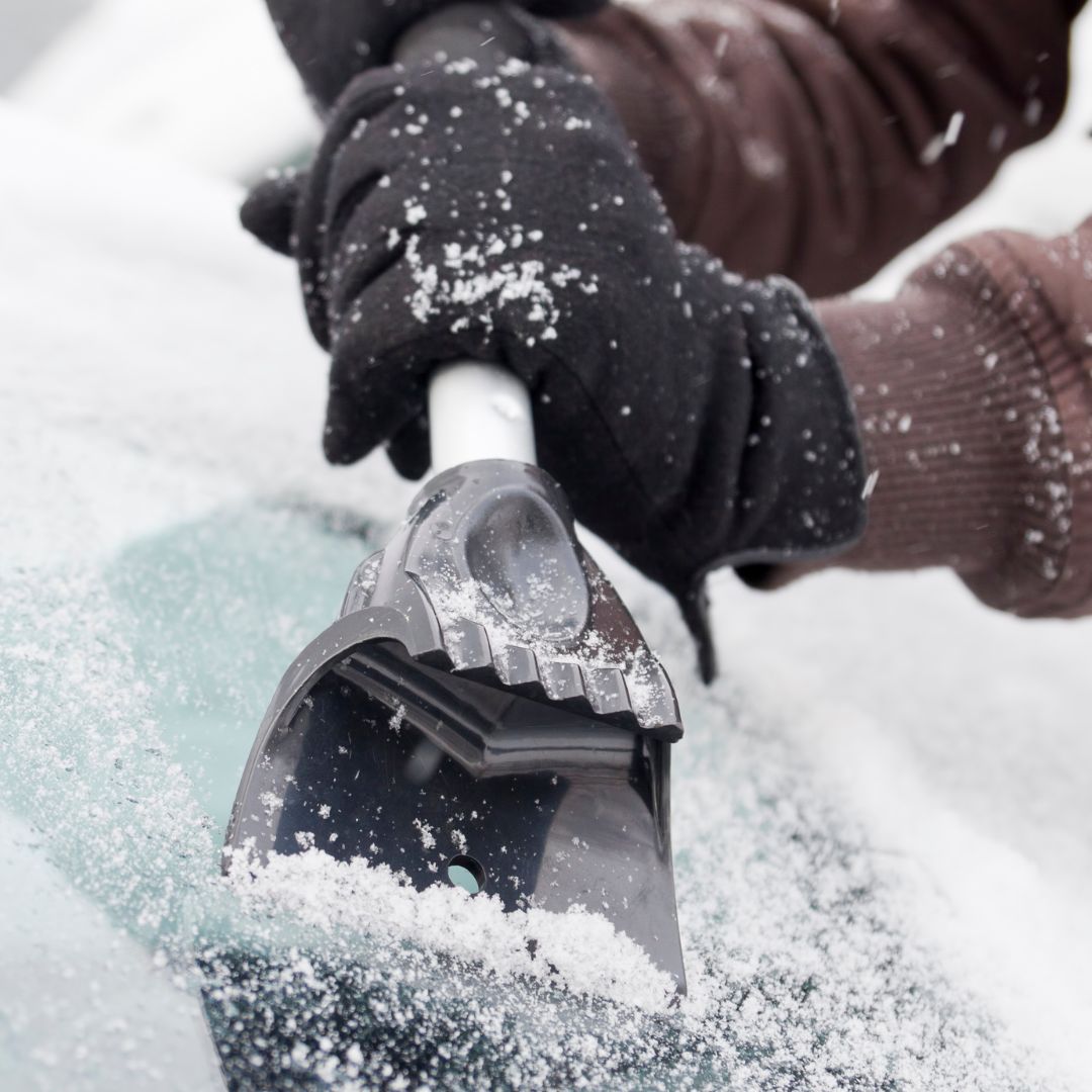 image of a driver scraping the windshield of a snow plow