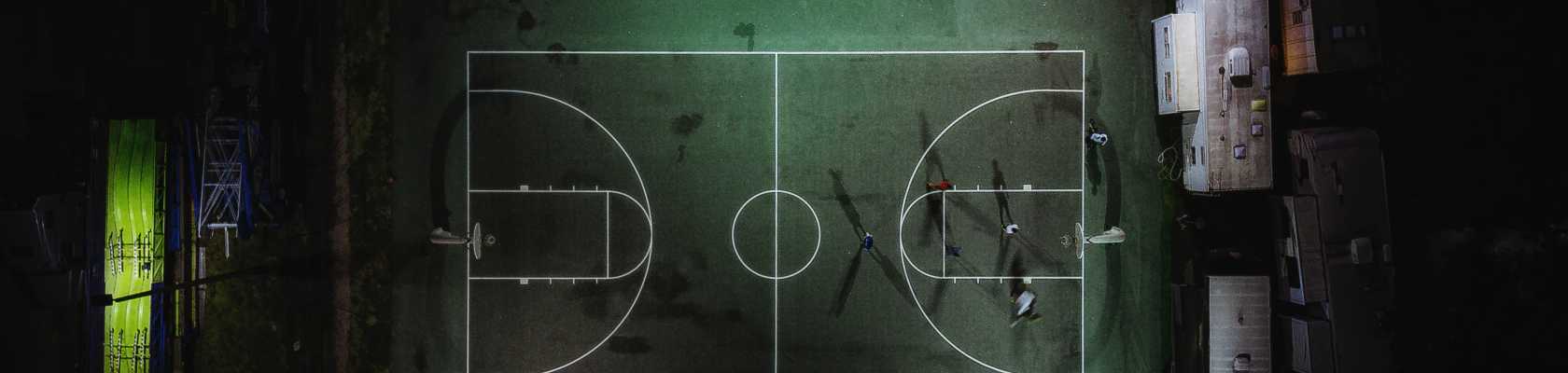 Overhead view of outdoor lights shining on a basketball court at night