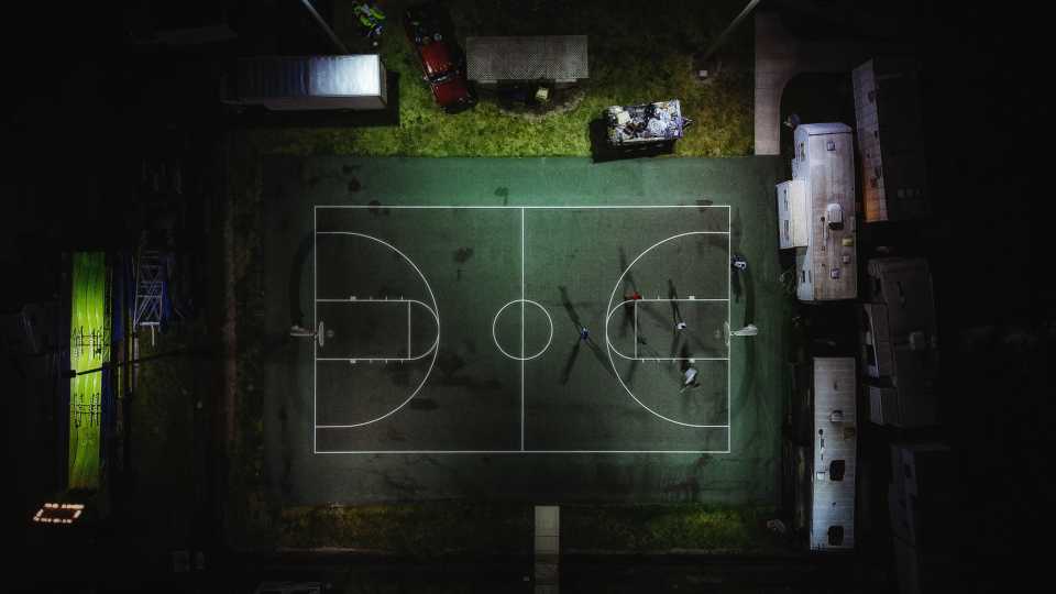Overhead view of outdoor lights shining on a basketball court at night